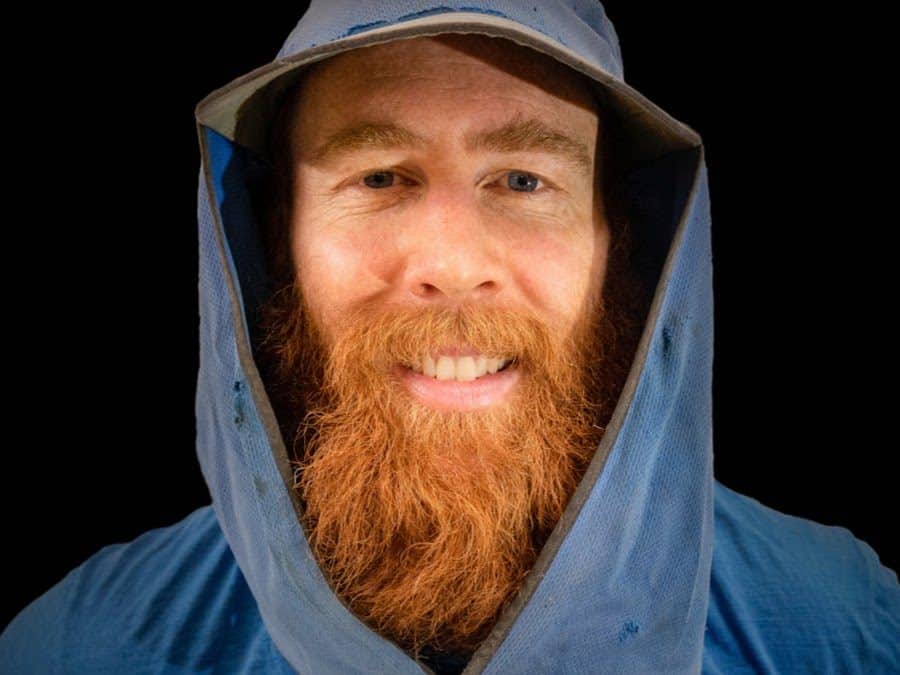 Photo of Beau Miles. Light blue sweater and hat. Long red beard.